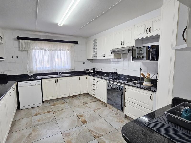 A functional kitchen featuring white cabinetry, dark granite countertops, tiled flooring, and built-in appliances including an oven, hob, and extractor fan.