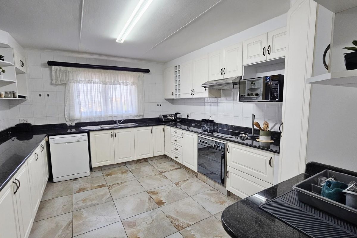 A functional kitchen featuring white cabinetry, dark granite countertops, tiled flooring, and built-in appliances including an oven, hob, and extractor fan.