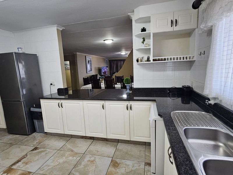 A functional kitchen featuring dark granite countertops, white cabinetry, and tiled flooring, seamlessly flowing into the adjacent dining and living area.