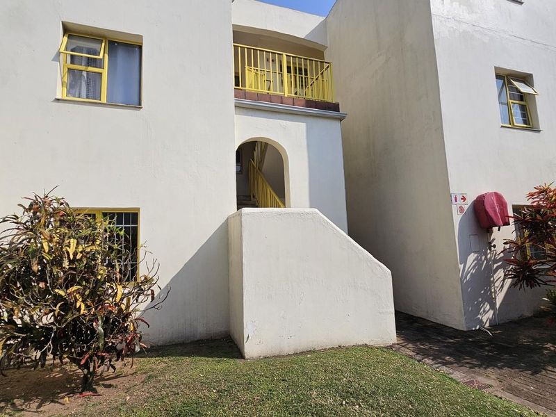 Exterior view of an apartment building featuring a central staircase, yellow metal railings, and paved walkway access.