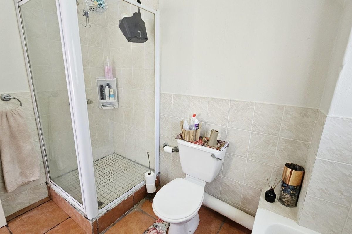 A functional bathroom featuring a glass-enclosed shower, a standard toilet, and tiled flooring with neutral wall finishes.