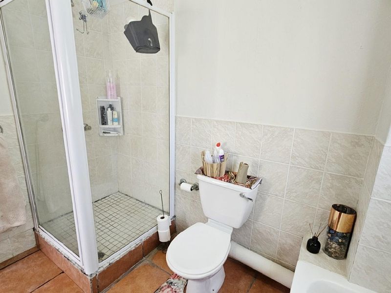 A functional bathroom featuring a glass-enclosed shower, a standard toilet, and tiled flooring with neutral wall finishes.