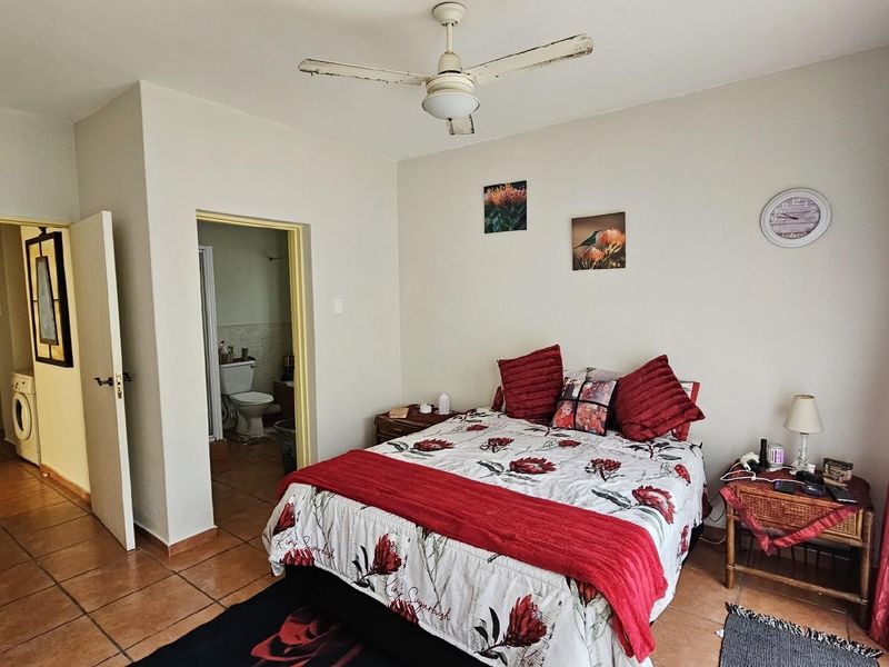 A bedroom featuring tiled flooring, a ceiling fan, and an adjoining bathroom, with a doorway leading to a laundry area.