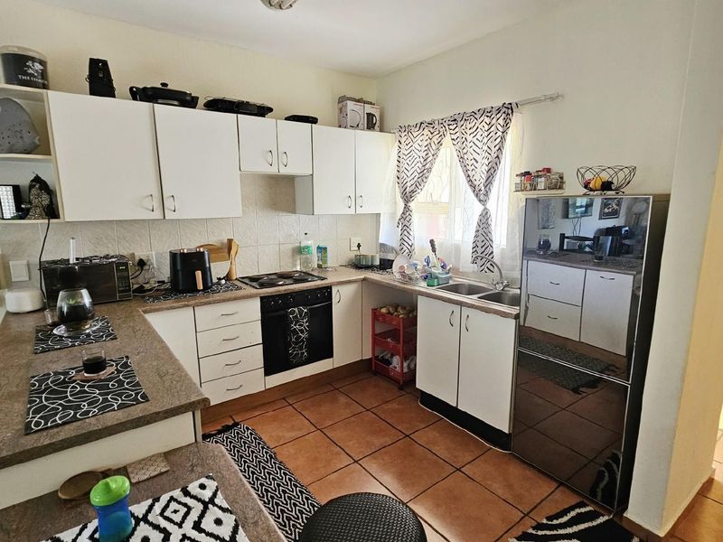 A functional kitchen featuring white cabinetry, a built-in oven and hob, tiled countertops, and terracotta floor tiles.