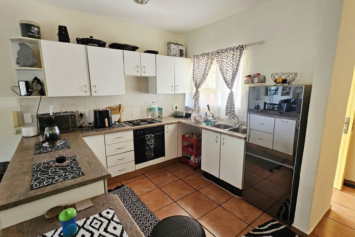 A functional kitchen featuring white cabinetry, a built-in oven and hob, tiled countertops, and terracotta floor tiles.