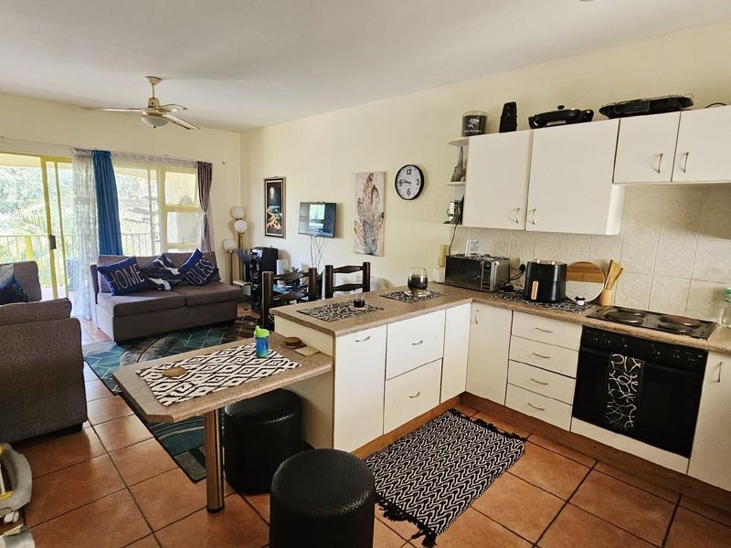 Open-plan living area featuring a functional kitchen with built-in oven and hob, flowing into a lounge space with direct access to a balcony.