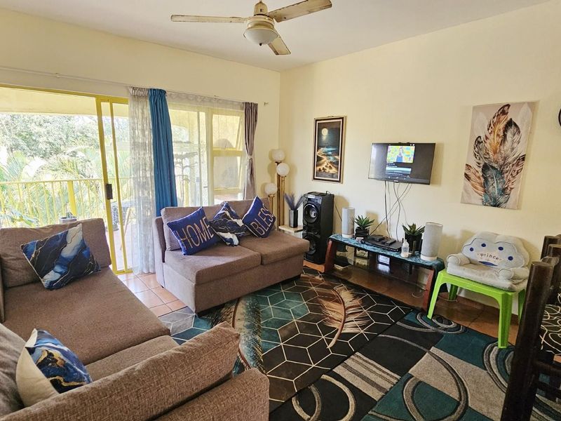 A comfortable living room featuring a ceiling fan and large sliding glass doors that provide access to an outdoor balcony area.