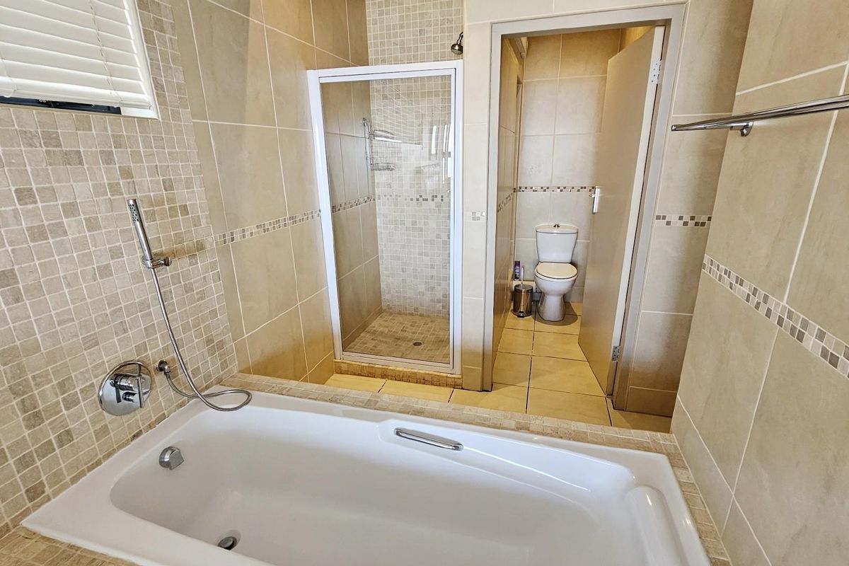 A well-maintained bathroom featuring a built-in bathtub, a separate glass-enclosed shower, and a private toilet area with neutral wall and floor tiling.