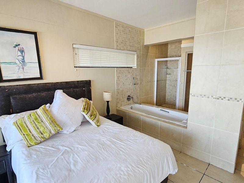 Open-plan bedroom featuring an integrated en-suite bathroom with a built-in bathtub and separate shower enclosure, finished with neutral ceramic tiling.