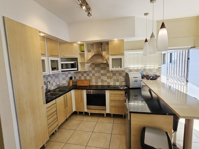 A functional kitchen featuring light wood cabinetry, black granite countertops, a built-in oven, extractor fan, and a breakfast bar counter.