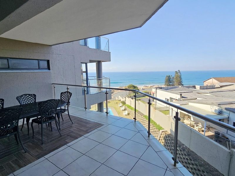 Spacious covered balcony featuring tiled flooring, glass balustrades, and panoramic ocean views, providing an ideal outdoor entertainment space.