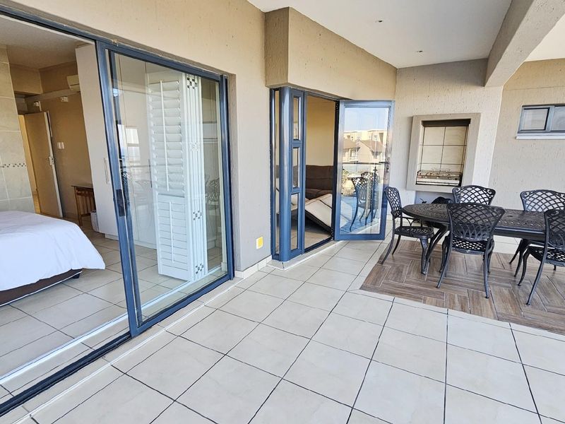 Spacious covered balcony featuring tiled flooring, a built-in braai, and large sliding glass doors providing seamless access to the interior living space.