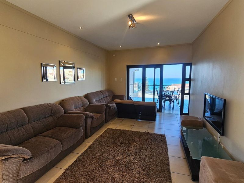 Spacious living area featuring tiled flooring and large glass sliding doors that open onto a balcony with scenic ocean views.