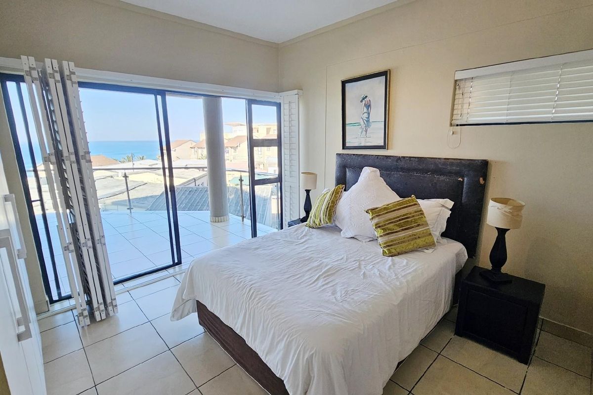 Bedroom featuring tiled flooring, built-in cupboards, and large sliding glass doors opening onto a balcony with ocean views.