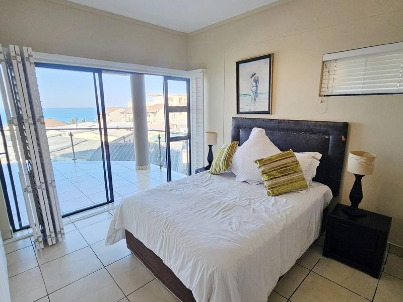 Bedroom featuring tiled flooring, built-in cupboards, and large sliding glass doors opening onto a balcony with ocean views.