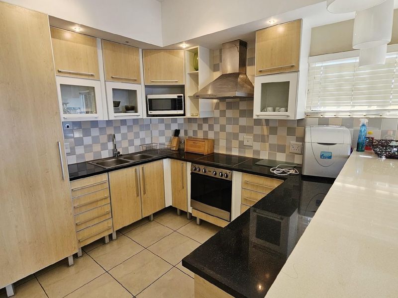 Modern kitchen featuring light wood cabinetry, black granite countertops, a stainless steel extractor fan, built-in oven, and a breakfast bar.