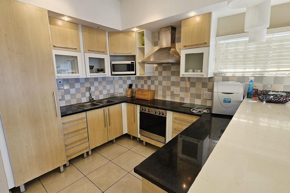 Modern kitchen featuring light wood cabinetry, black granite countertops, a stainless steel extractor fan, built-in oven, and a breakfast bar.