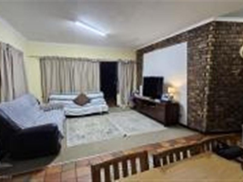 Open plan living and dining area featuring a prominent exposed brick feature wall and tiled flooring.