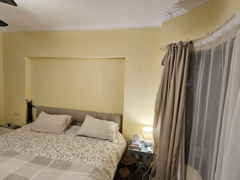 A bedroom featuring a recessed wall niche, ceiling fan, and large window with curtain tracks.
