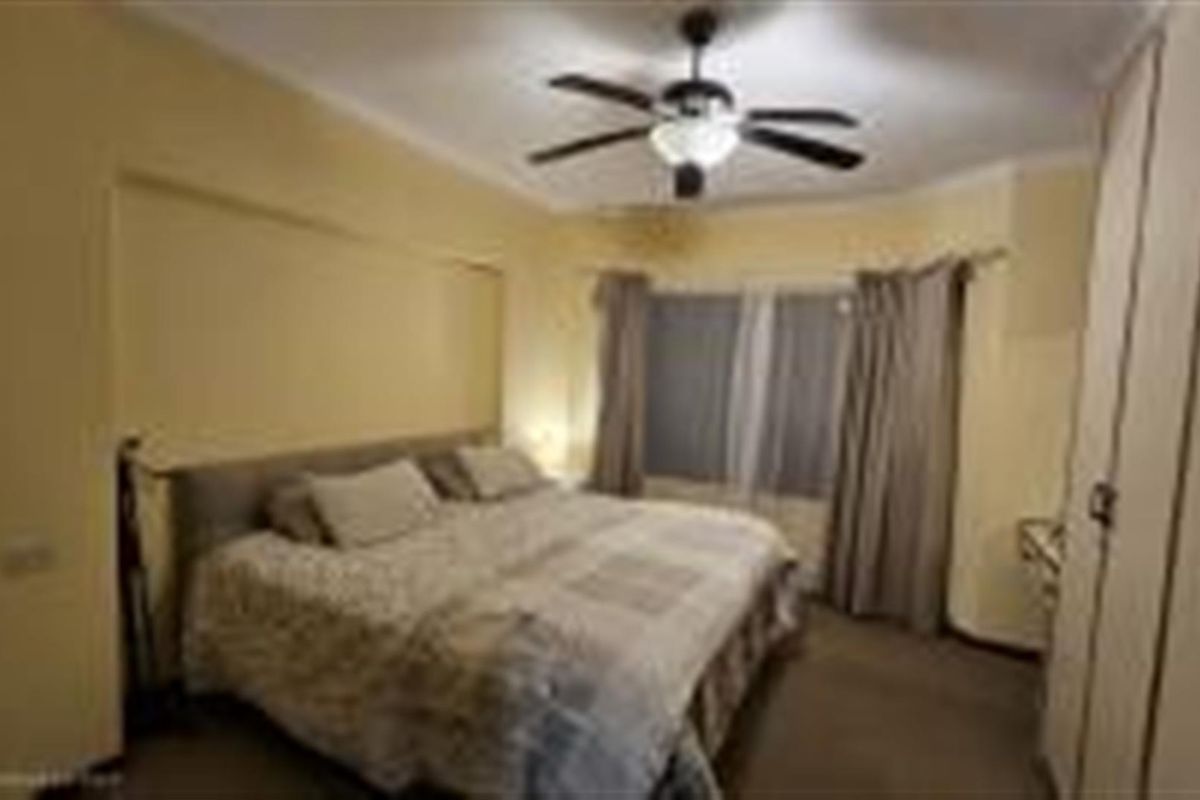 A spacious bedroom featuring built-in cupboards, a ceiling fan, and neutral wall finishes, providing a comfortable and functional living space.