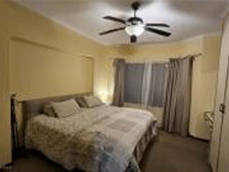 A spacious bedroom featuring built-in cupboards, a ceiling fan, and neutral wall finishes, providing a comfortable and functional living space.