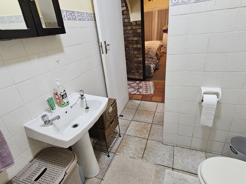 A functional bathroom featuring a pedestal basin, tiled walls, and floor, with a view into the adjacent bedroom area.