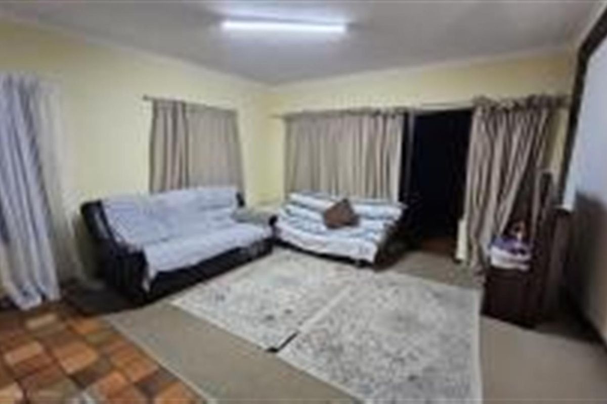 A living room area featuring mixed flooring, including tiled and carpeted sections, with access to an outdoor space through sliding doors.