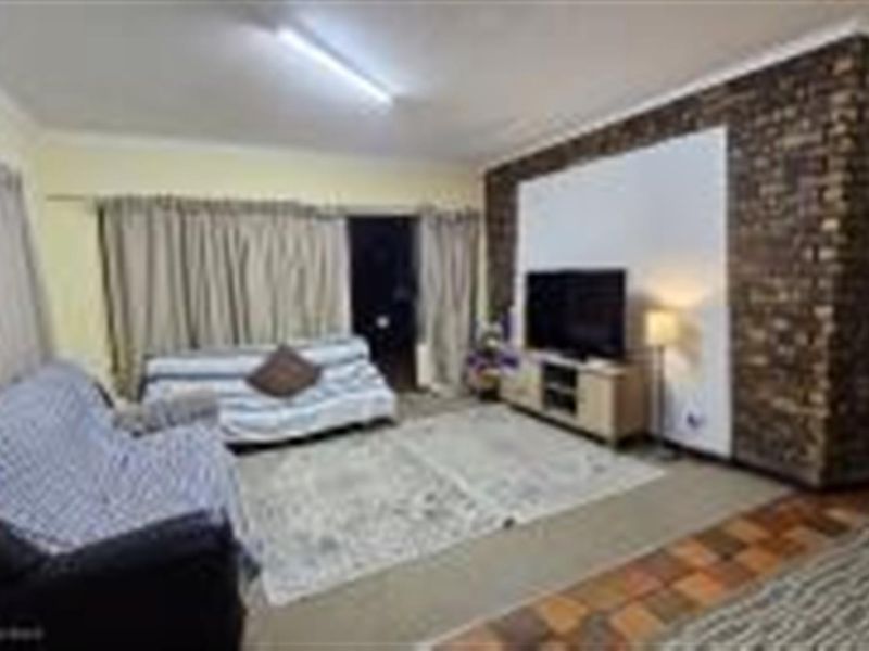 A living room featuring a prominent exposed brick feature wall, tiled flooring, and sliding door access to the exterior.