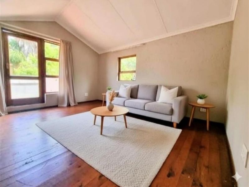 A bright living room featuring vaulted ceilings, rich timber flooring, and large windows that provide ample natural light and garden views.