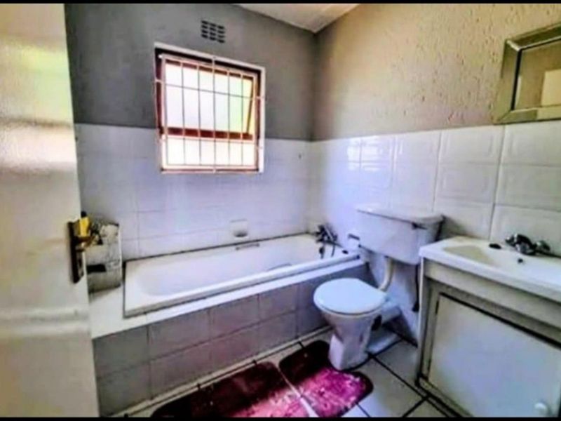 A compact bathroom featuring a built-in bathtub, a standard toilet, and a vanity basin with tiled walls and security bars on the window.