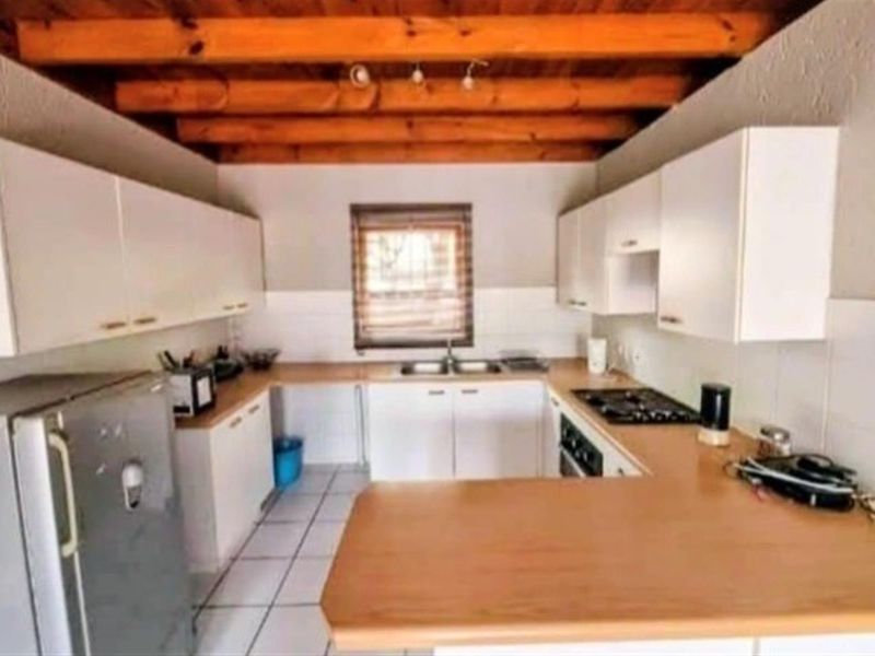A functional kitchen featuring white cabinetry, wood-look laminate countertops, a built-in gas hob, and exposed timber ceiling beams.