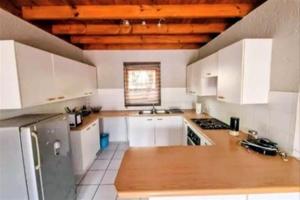 A functional kitchen featuring white cabinetry, wood-look laminate countertops, a built-in gas hob, and exposed timber ceiling beams.