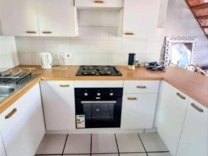 Compact kitchen featuring white cabinetry, wood-look laminate countertops, a built-in oven, and a four-plate electric hob with tiled flooring.