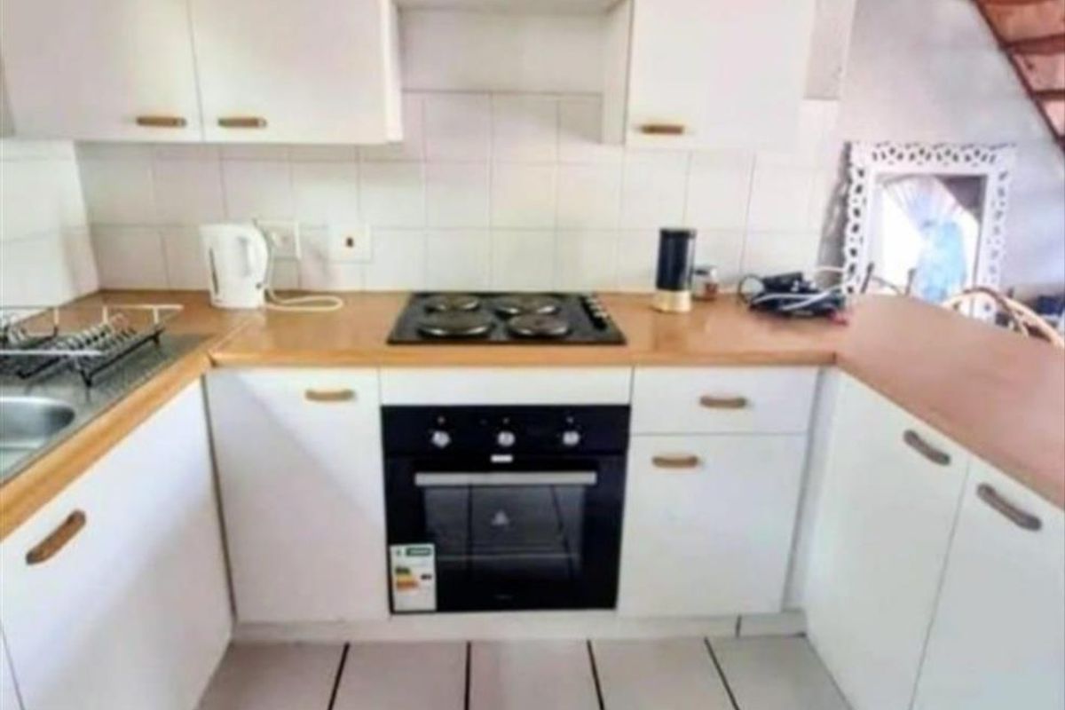 Compact kitchen featuring white cabinetry, wood-look laminate countertops, a built-in oven, and a four-plate electric hob with tiled flooring.