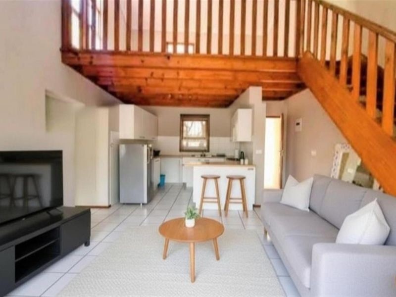 Open-plan living area featuring a kitchen with built-in cabinetry, tiled flooring, and a wooden staircase leading to an upper mezzanine level.