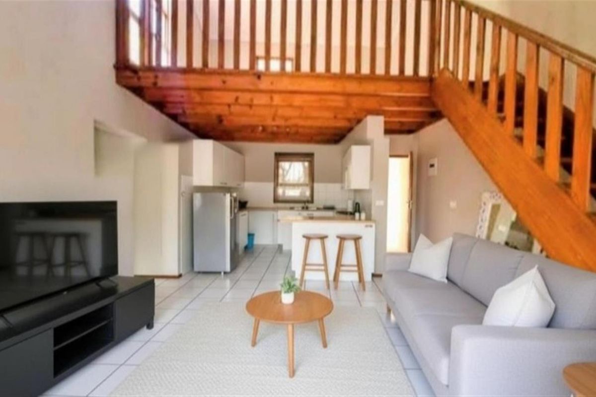 Open-plan living area featuring a kitchen with built-in cabinetry, tiled flooring, and a wooden staircase leading to an upper mezzanine level.
