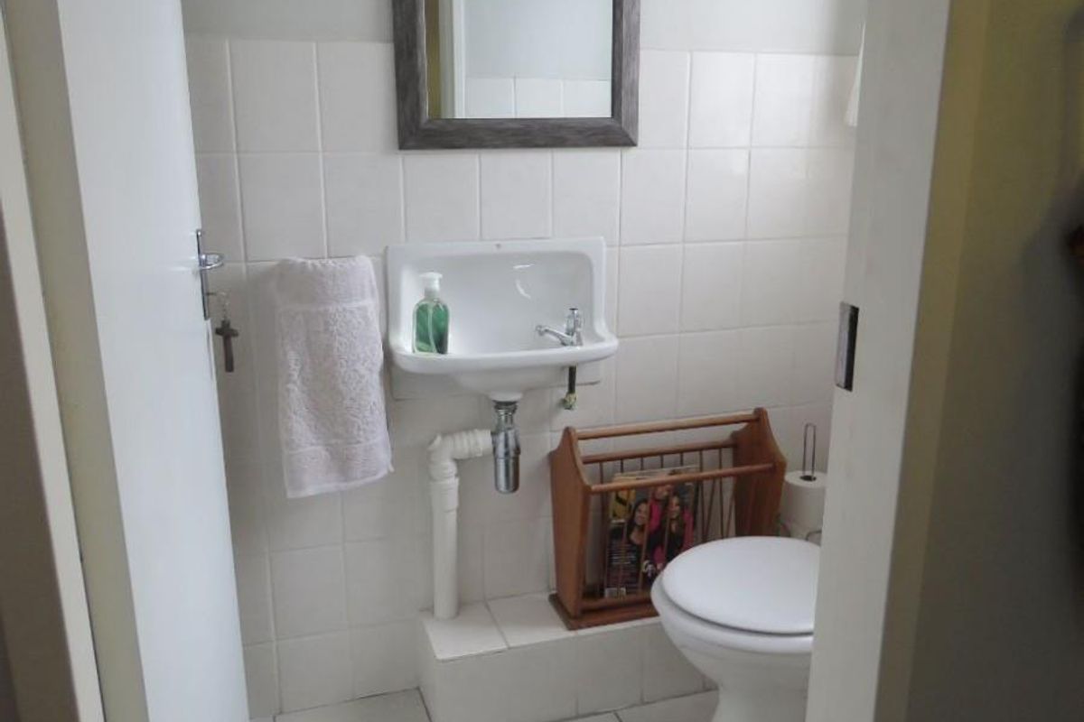 A compact guest bathroom featuring a wall-mounted basin, tiled splashback, and a standard toilet.