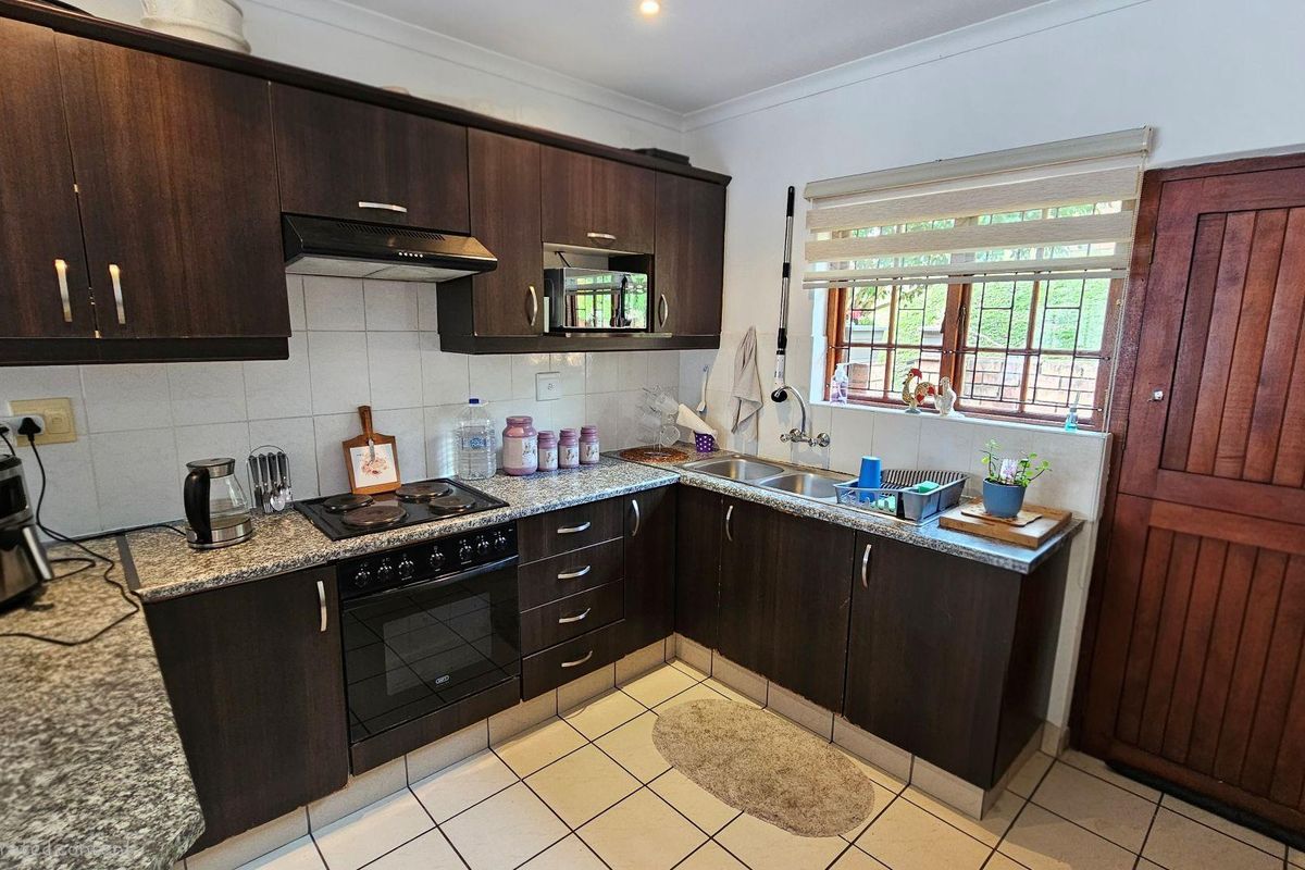 A functional kitchen featuring dark wood cabinetry, granite countertops, a built-in oven with hob, extractor fan, and a double stainless steel sink.
