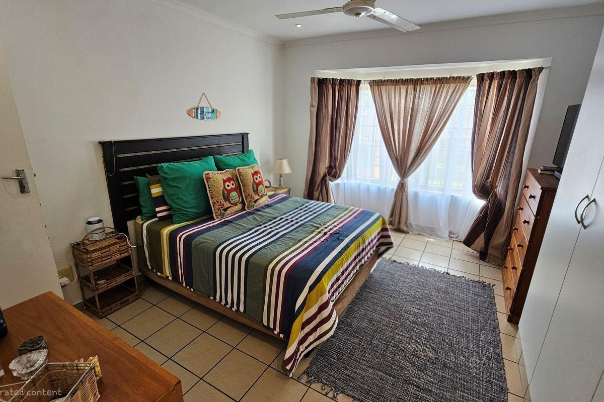 A well-lit bedroom featuring tiled flooring, a ceiling fan, and a large bay window with curtains.