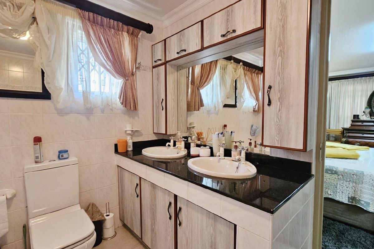 Bathroom featuring a double vanity with granite countertops, integrated sinks, and wood-look cabinetry, adjacent to a toilet and tiled wall finishes.