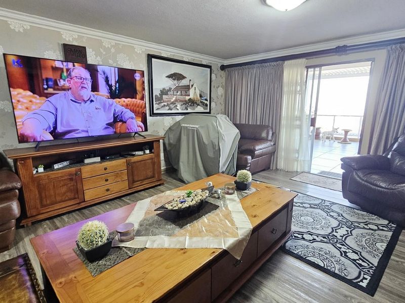 A comfortable living room featuring wood-look flooring, patterned wallpaper, and sliding glass doors that open onto a private balcony.