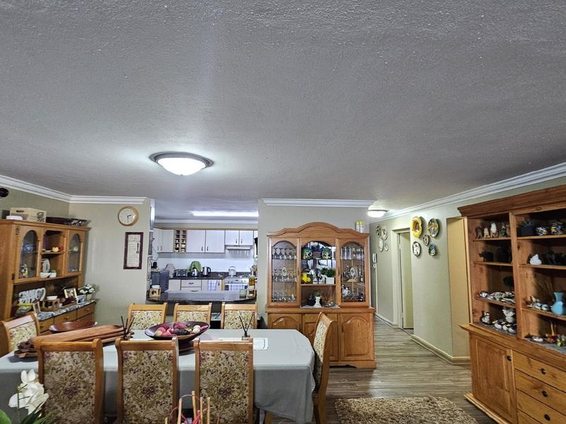 Open plan living and dining area featuring crown molding, wood-look flooring, and a connected kitchen with built-in cabinetry.