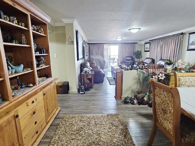 Spacious open-plan living and dining area featuring wood-look laminate flooring, crown molding, and sliding glass doors leading to an outdoor balcony.
