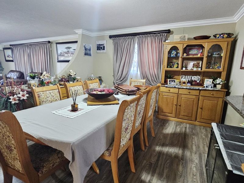 Open plan dining area featuring wood-look flooring, crown molding, and a seamless transition into the adjacent living space.