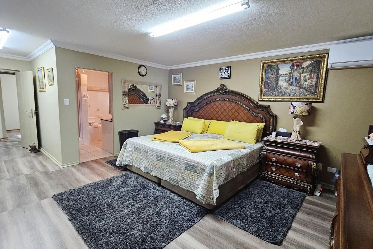 Spacious bedroom featuring wood-look laminate flooring, an en-suite bathroom, and a wall-mounted air conditioning unit.