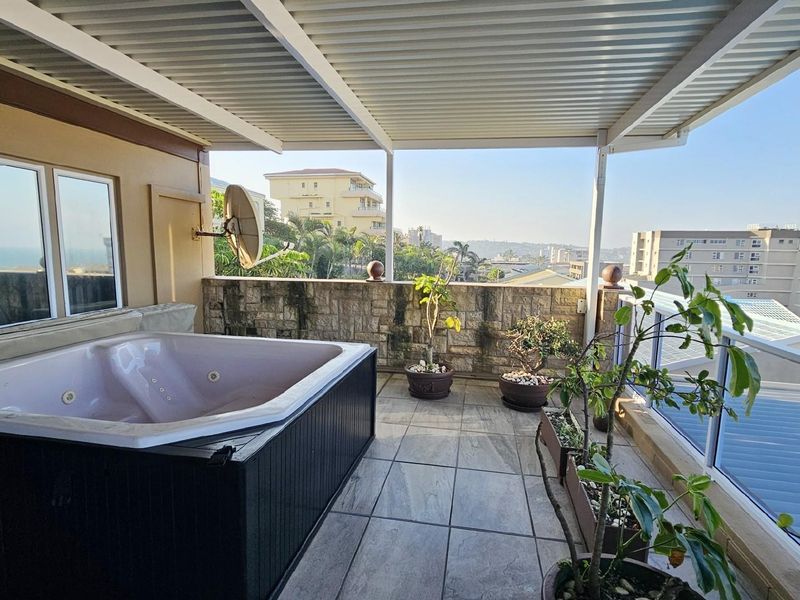 Covered balcony featuring a built-in spa bath, stone-clad feature wall, and tiled flooring, offering elevated views of the surrounding area.