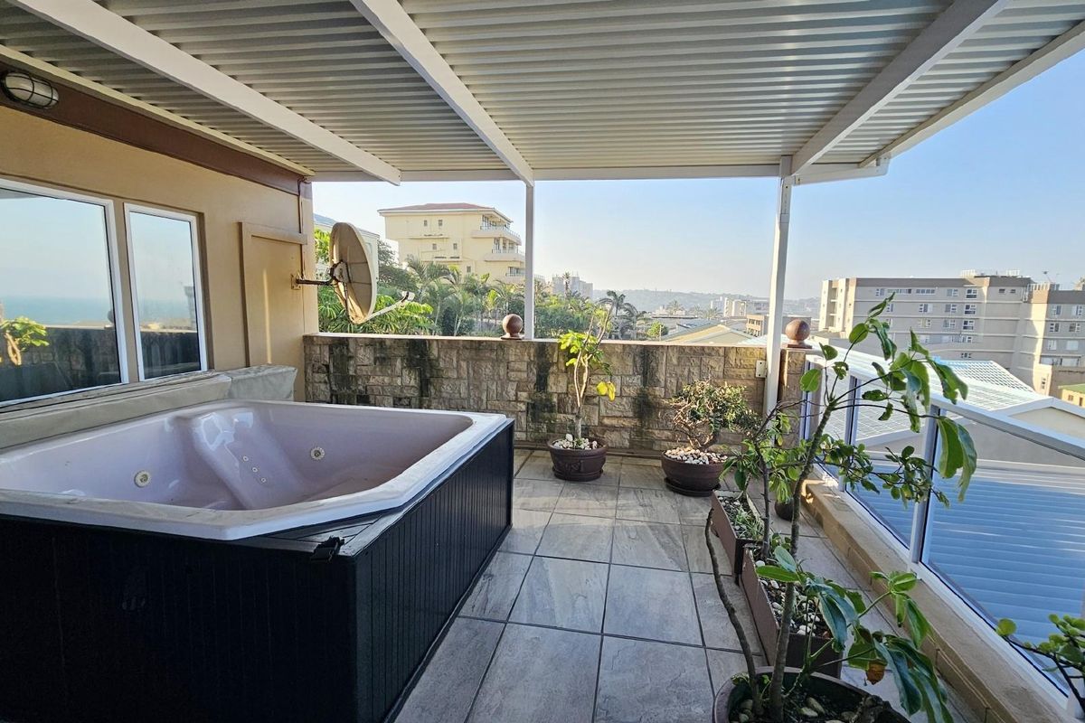 Covered balcony featuring a built-in spa bath, stone-clad feature wall, and tiled flooring, offering elevated views of the surrounding area.