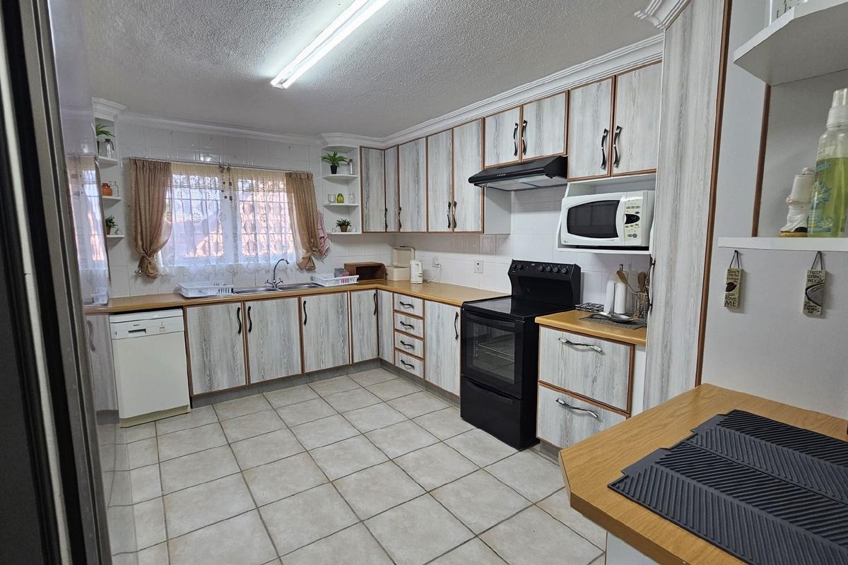 A functional kitchen featuring wood-grain laminate cabinetry, tiled flooring, a built-in oven with extractor fan, and a double-basin sink.