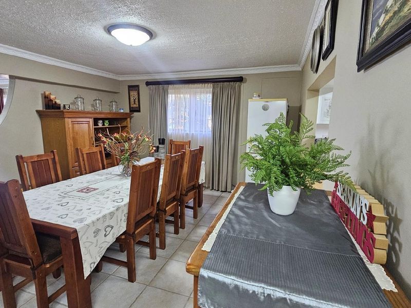 A dining room area featuring tiled flooring, decorative ceiling cornices, and a large window with curtains, providing a functional space for family meals.