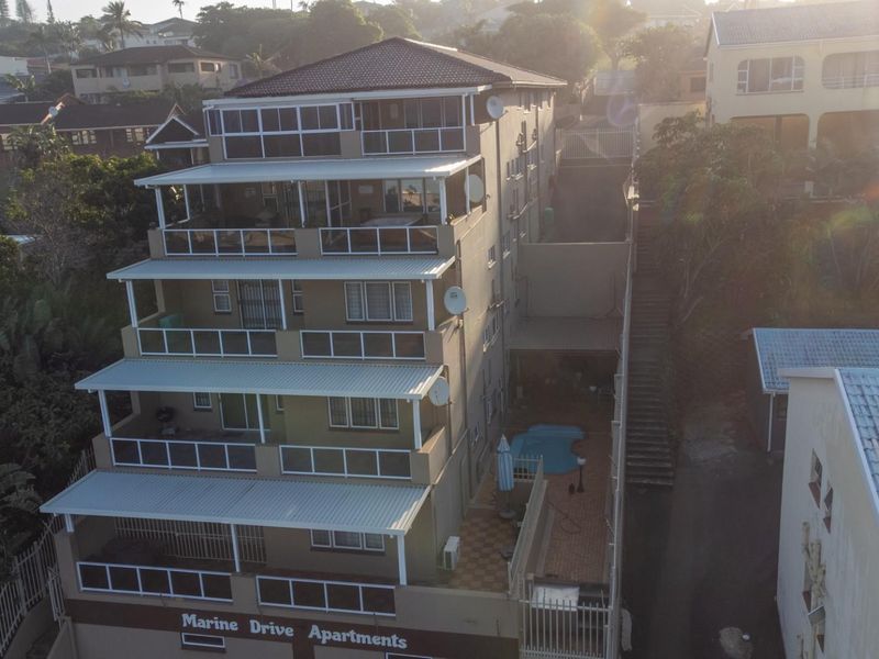 Aerial view of a multi-story apartment complex featuring private balconies, a ground-level swimming pool, and paved outdoor areas.